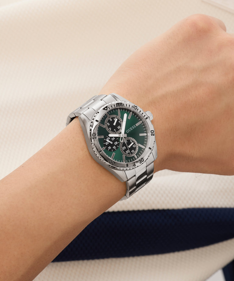 Silver watch with a green face on a wrist against a neutral background