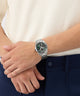 Person wearing a silver watch with a green face on a white background