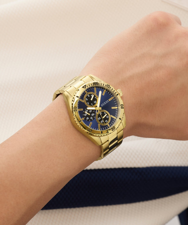 Gold wristwatch with a blue face on a wrist, against a neutral background