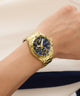 Gold wristwatch with a blue face on a wrist, against a neutral background