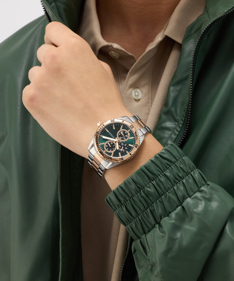 Person wearing a silver watch with a green face on a blurred background