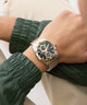 Close-up of a wrist wearing a silver and rose gold watch with a green strap.