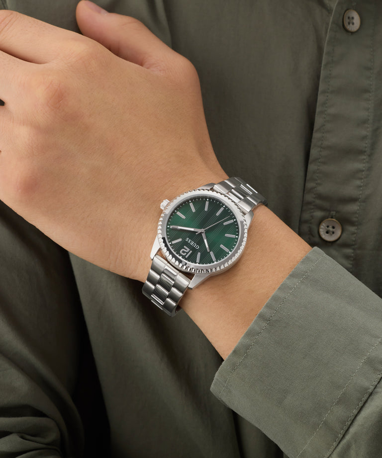 Hand wearing a silver GUESS Mens Silver Tone Analog Watch with a green face on a person wearing a green shirt.