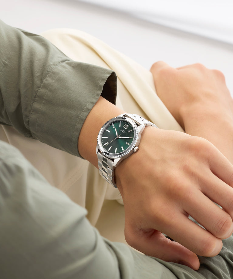 Person wearing a silver GUESS Mens Silver Tone Analog Watch with a green dial on a light background