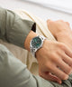 Person wearing a silver GUESS Mens Silver Tone Analog Watch with a green dial on a light background