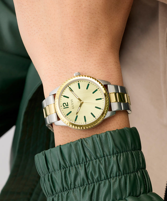 Gold and silver GUESS Mens 2-Tone Analog Watch on a wrist with a blurred background