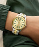 Gold and silver GUESS Mens 2-Tone Analog Watch on a wrist with a green jacket