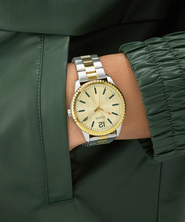 Gold and silver GUESS Mens 2-Tone Analog Watch on a wrist with a green jacket background