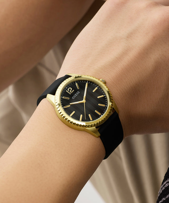Gold and black GUESS Mens Black Gold Tone Analog Watch on a wrist with a neutral background