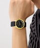 Gold and black GUESS Mens Black Gold Tone Analog Watch on a wrist with a neutral background