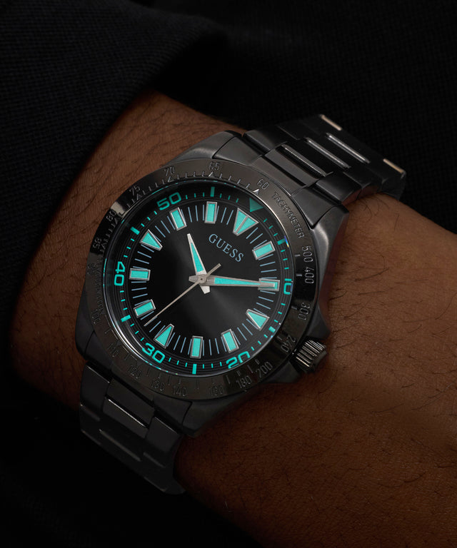 Black Guess watch with turquoise accents on a wrist against a dark background