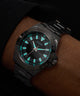 Black Guess watch with turquoise accents on a wrist against a dark background