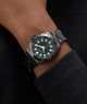 Black wristwatch with blue accents on a person's wrist against a dark background