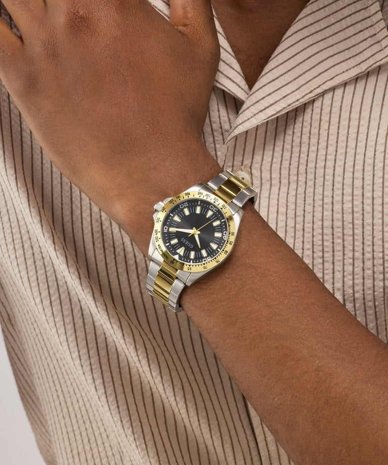 Gold and silver watch on a wrist with a neutral background