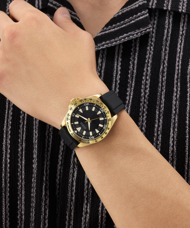 Gold watch with black strap on a wrist against a striped background