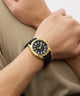 Person wearing a black and gold watch on a beige background