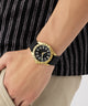 Gold watch with black strap on a wrist against a blurred background