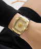 Gold GUESS Mens Black Gold Tone Analog Watch with black strap on a wrist against a neutral background