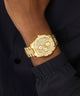 Gold wristwatch with detailed design on a person's wrist against a dark background