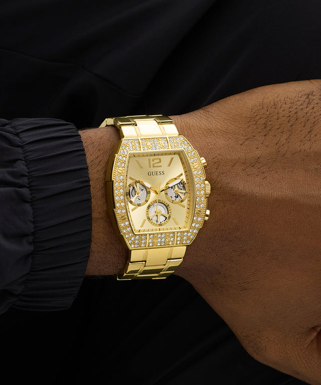 Gold GUESS Mens Gold Tone Analog Watch with diamond accents on a wrist against a black background