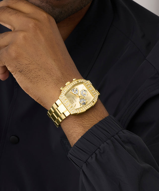 Gold GUESS Mens Gold Tone Analog Watch with diamond accents on a person wearing a black outfit.
