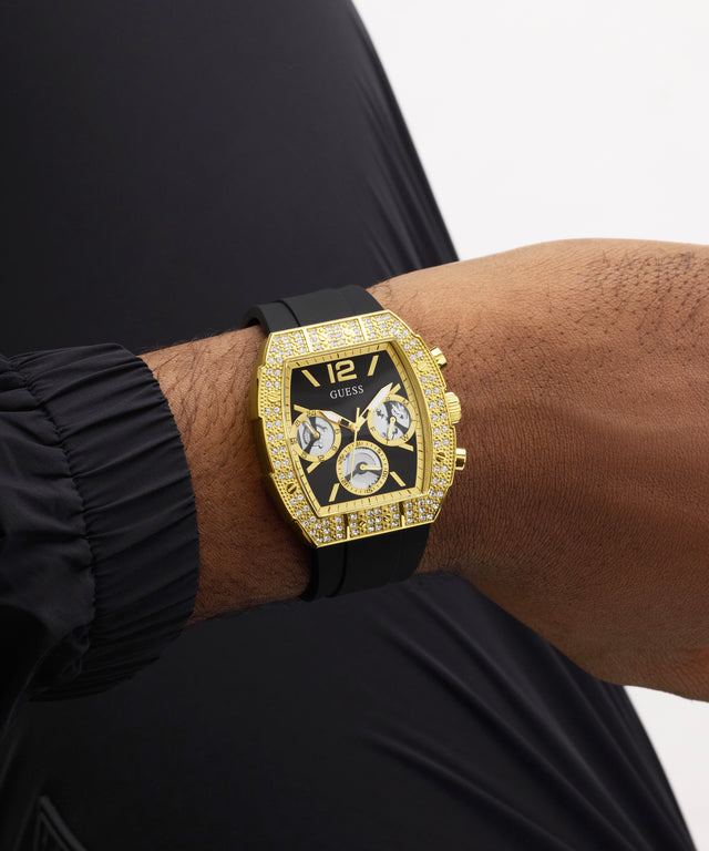 Gold GUESS Mens Black Gold Tone Analog Watch with black strap on a wrist against a neutral background
