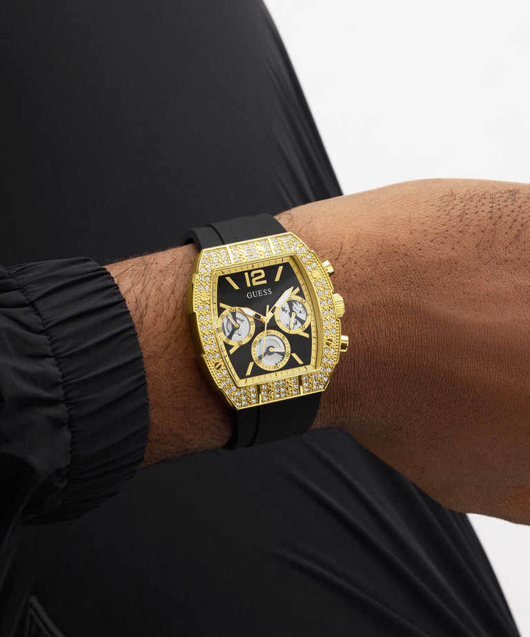 Gold GUESS Mens Black Gold Tone Analog Watch with black strap on a wrist against a neutral background