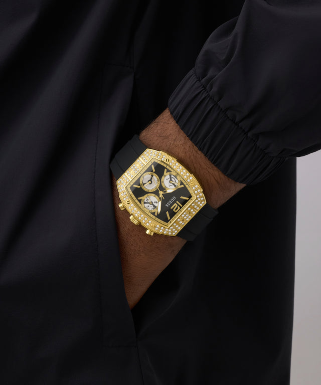 GUESS Mens Black Gold Tone Analog Watch with diamond accents on a person's wrist against a black background