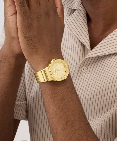 Gold GUESS Mens Jaq Gold Tone Analog Watch on a wrist with a neutral background