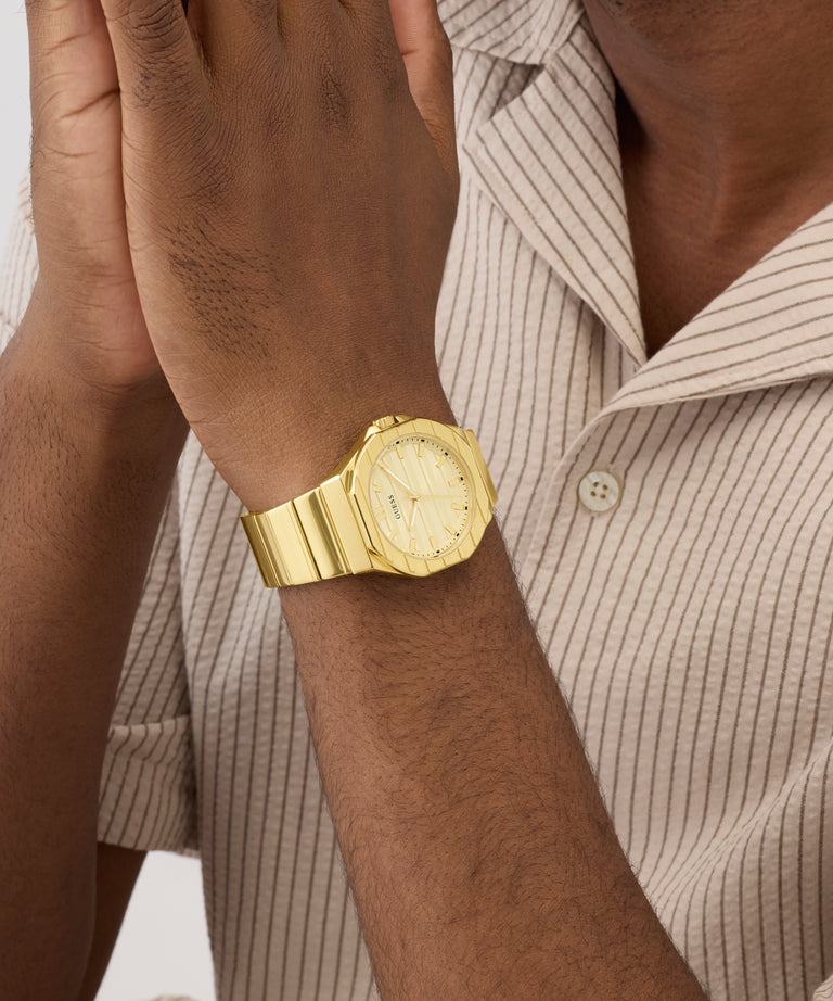 Gold GUESS Mens Jaq Gold Tone Analog Watch on a wrist with a neutral background