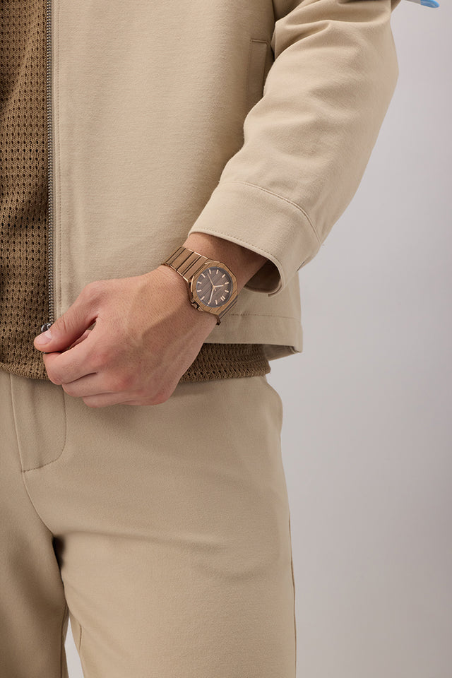 Person wearing a beige jacket and pants with a GUESS Mens Jaq Coffee Analog Watch on a plain background