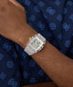 Silver watch on a wrist with a dark blue fabric background
