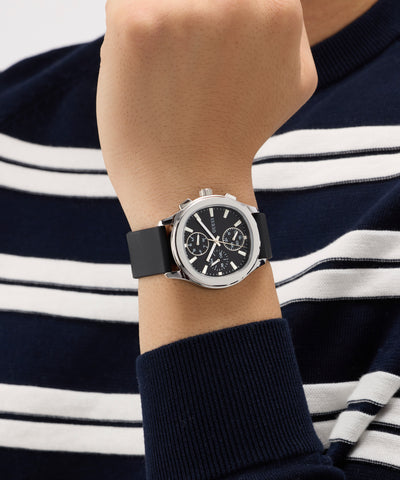 Person wearing a black GUESS Mens Palmer Black Silver Tone Analog Watch with a navy and white striped shirt