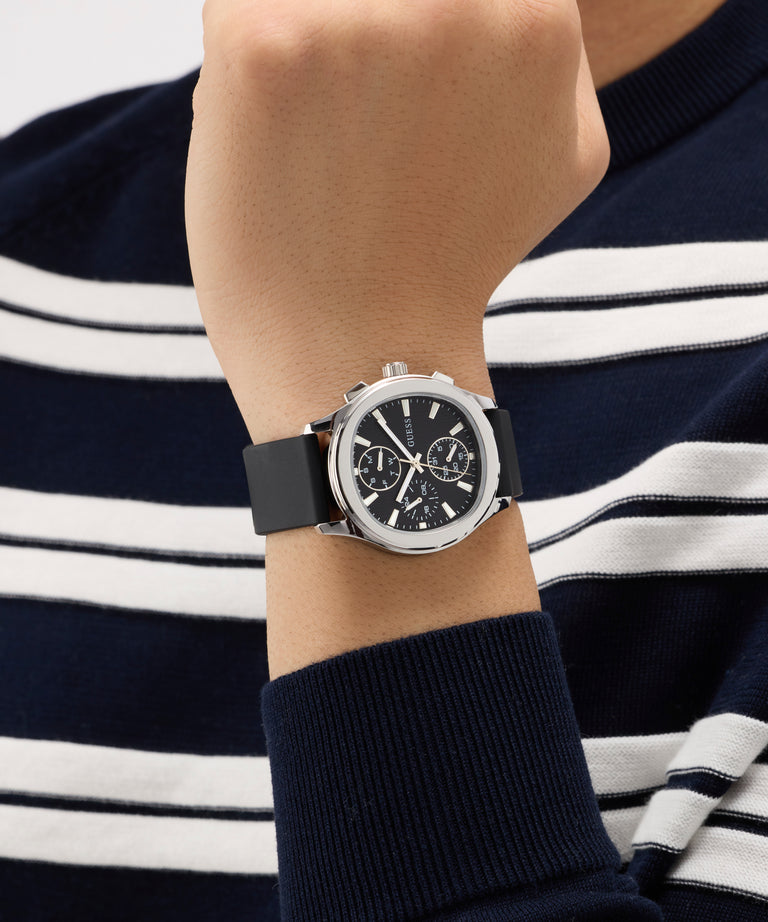 Person wearing a black GUESS Mens Palmer Black Silver Tone Analog Watch with a navy and white striped shirt