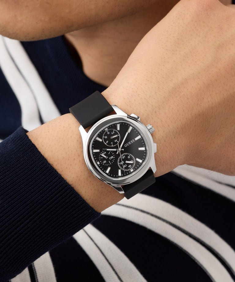 Close-up of a person wearing a GUESS Mens Palmer Black Silver Tone Analog Watch watch with a black strap.