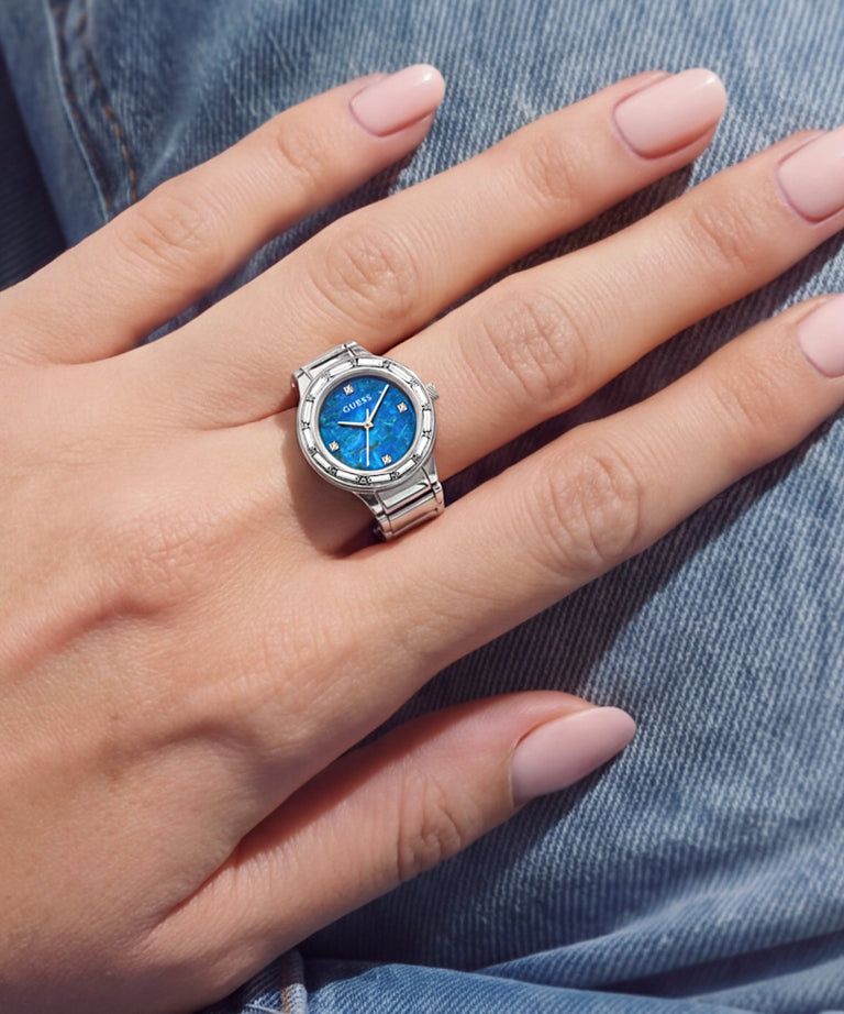 A silver-toned ring with a blue dial and clear stones, worn on a person's hand.