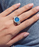 A silver-toned ring with a blue dial and clear stones, worn on a person's hand.