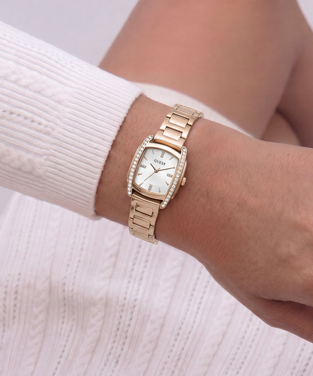 A gold-tone women's watch with a white dial and crystal accents, shown on a model's wrist wearing a white ribbed knit sweater.