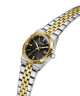 A two-tone Guess women's watch with a silver and gold stainless steel link bracelet, a gold fluted bezel, and a black dial with gold hands and indices. lifestyle