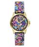 A Guess wristwatch with a gold-tone case and a colorful Day of the Dead patterned strap and dial, featuring sugar skulls, flowers, and butterflies on a white background.