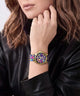 A close-up of a woman wearing a colorful wristwatch with a gold-tone case and a vibrant floral patterned strap, paired with a black leather jacket.