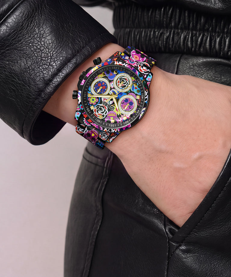 A close-up of a wrist wearing a colorful, highly detailed watch with a black leather jacket sleeve and black leather pants.