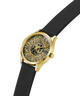 A wristwatch with a gold-tone case, a black textured dial featuring a sunburst pattern and the Guess logo, and a black strap, shown on a plain white background. lifestyle
