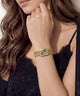 A close-up lifestyle shot of a woman wearing a gold-toned rectangular watch with a colorful floral enamel face and a matching chain bracelet.