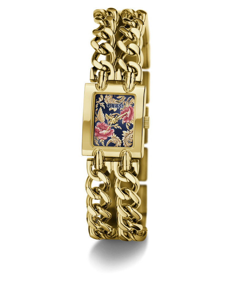 A gold-tone GUESS watch with a thick chain-link bracelet and a rectangular face featuring a navy blue background with pink and gold floral details.