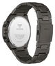 The back view of a GUESS stainless steel watch with a dark gunmetal gray case and integrated metal link bracelet, showing the branded crystal cover.