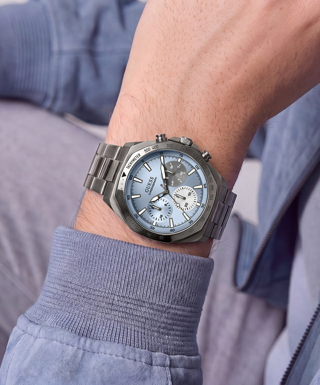 A wristwatch with a silver-toned metal bracelet and a light blue dial, worn on a person's wrist. The watch has three subdials and a silver case.