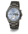 A GUESS chronograph watch with a dark gunmetal gray stainless steel case and link bracelet, featuring a light blue dial with white and black sub-dials.
