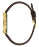 A side profile view of a watch with a gold-tone case and a dark brown leather strap, shown against a solid white background.