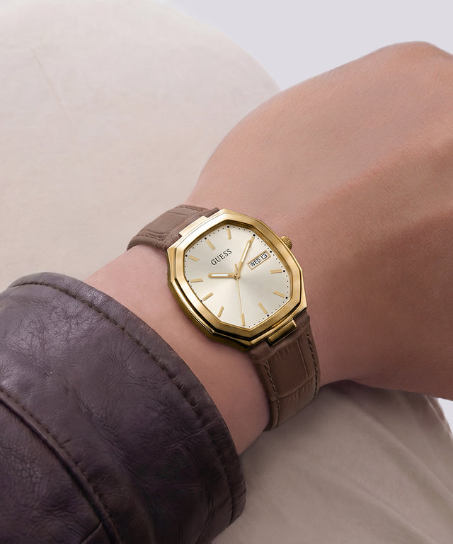A wristwatch with a gold-tone octagonal bezel, cream dial, and brown leather strap, shown worn on a person's wrist.